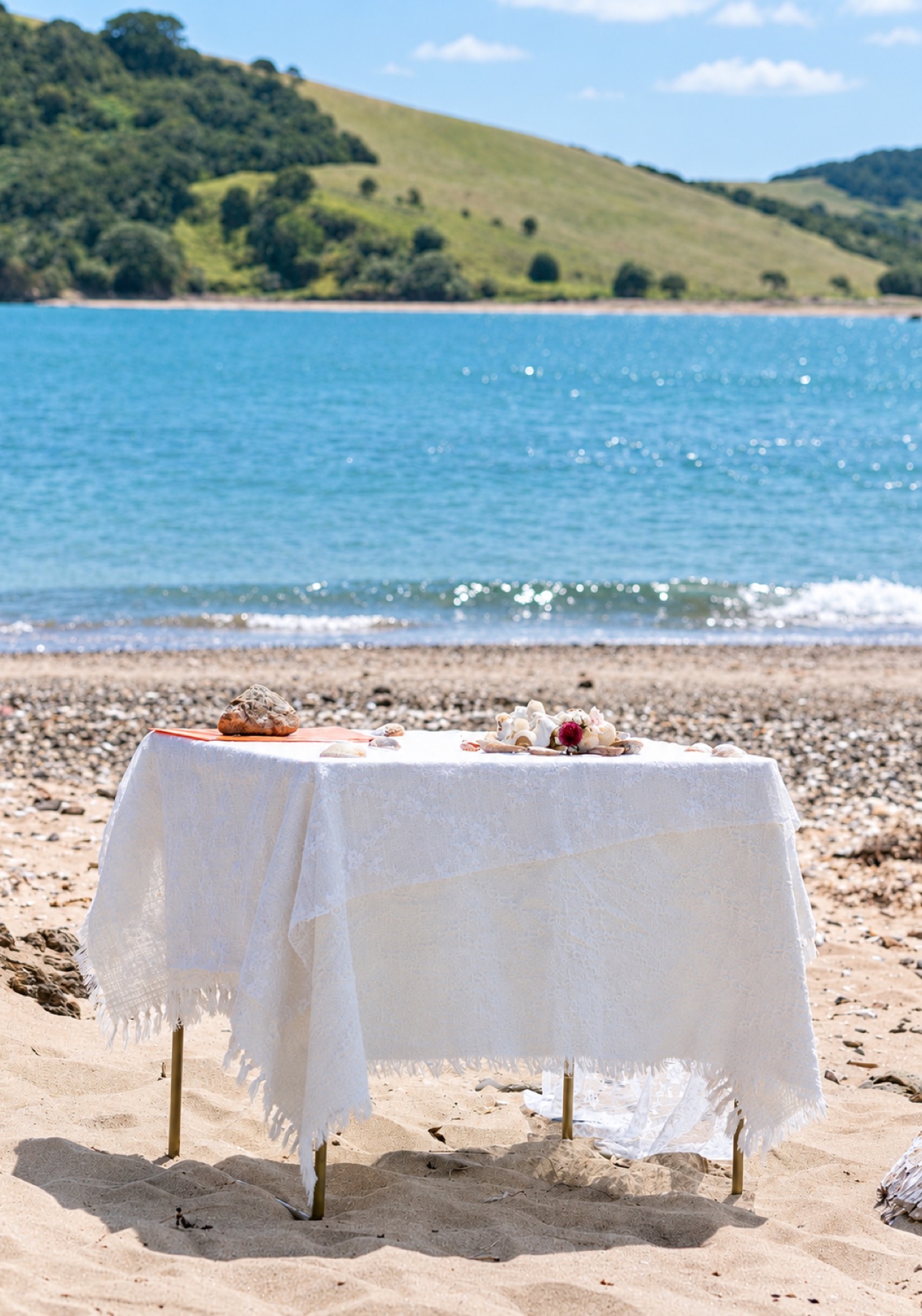 A white ceremony table decorated with shells beside the bay