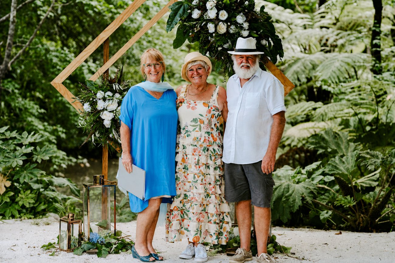Chris standing with a couple in front of a floral arch surrounded by ferns