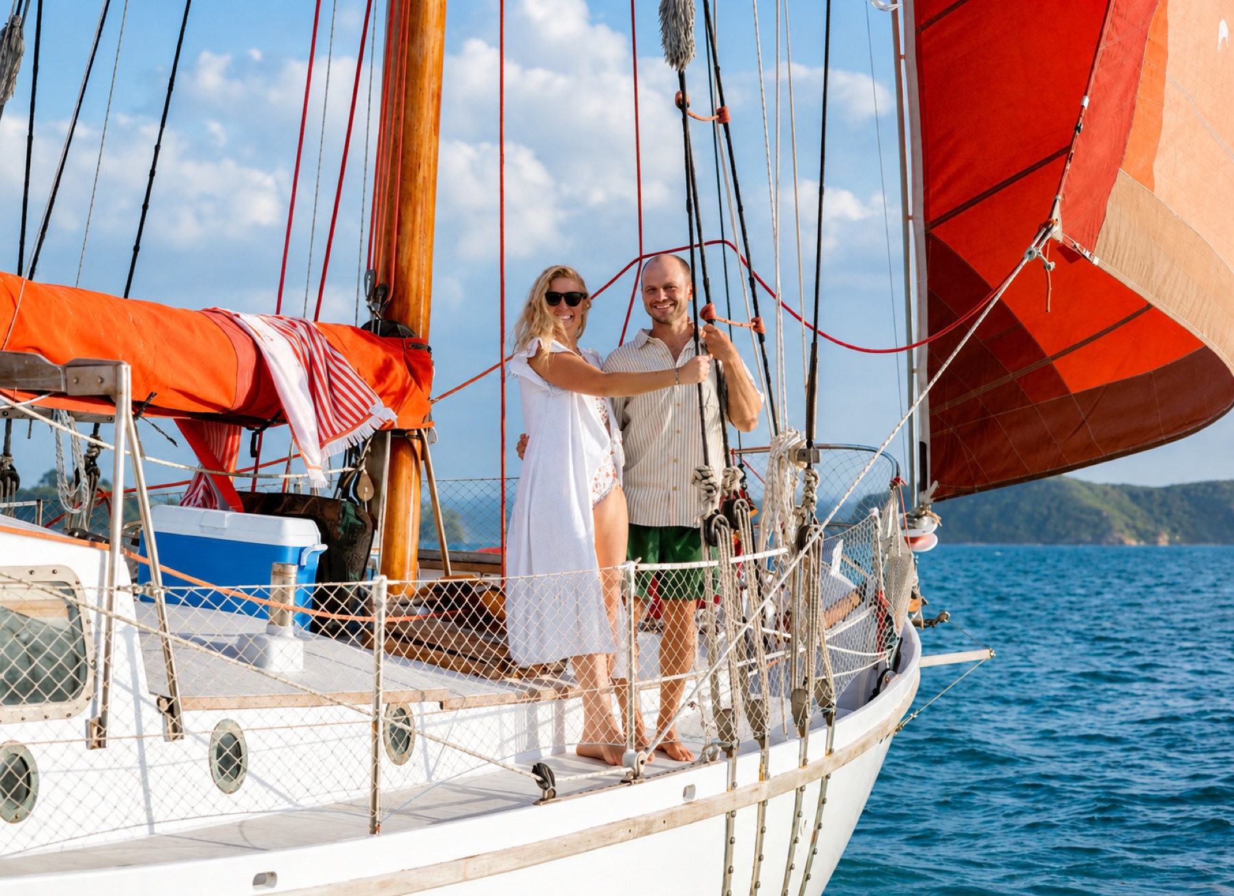 A couple celebrating aboard a sailing boat with red sails
