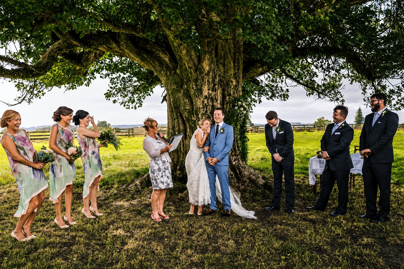 A full wedding party gathered for a ceremony beneath a large tree