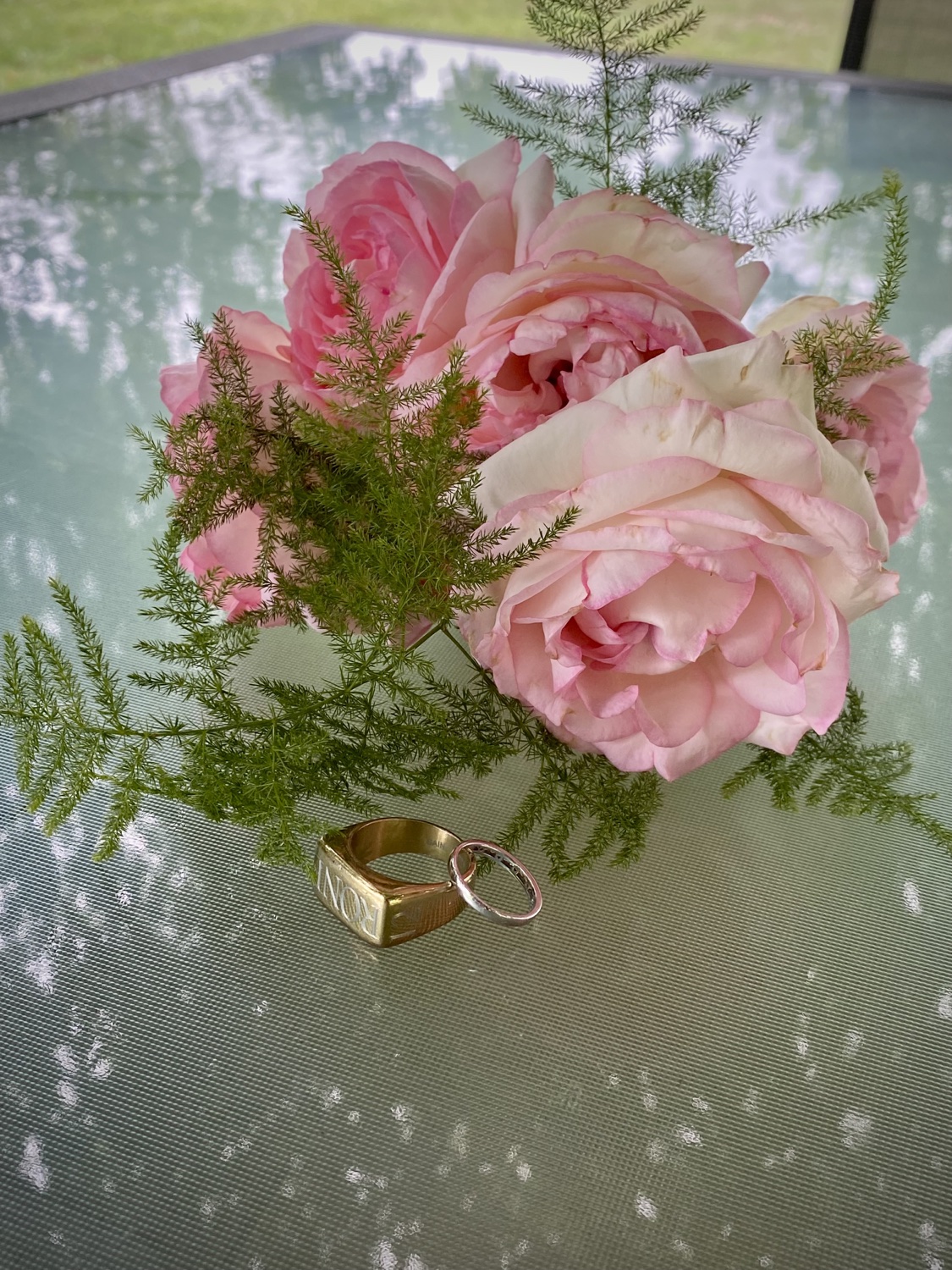 Two wedding rings and pink flowers on a glass table
